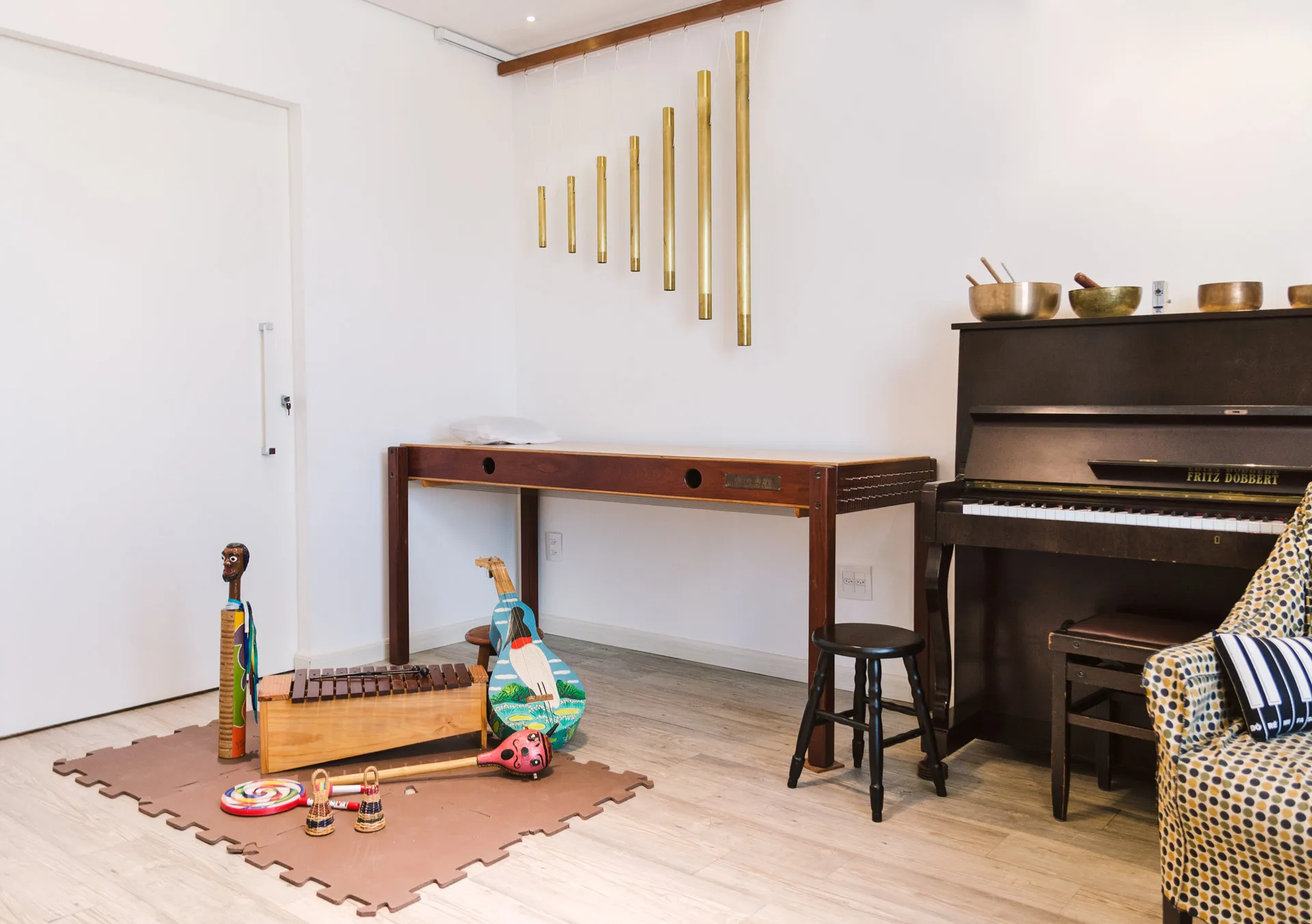 Sala de musicoterapia com piano, tubos sonoros na parede e instrumentos musicais no chão
